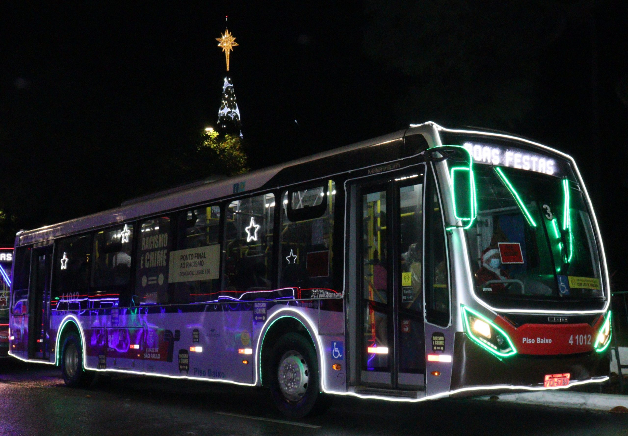 Ônibus com plotagem da campanha Ponto Final ao Racismo, ao fundo a árvore de natal do Parque do Ibirapuera